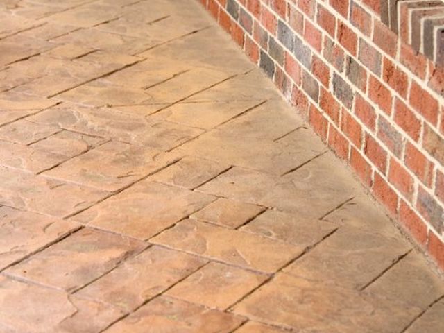 Porche de hormigón impreso molde piedra irregular en tono terracota junto a fachada de ladrillo visto